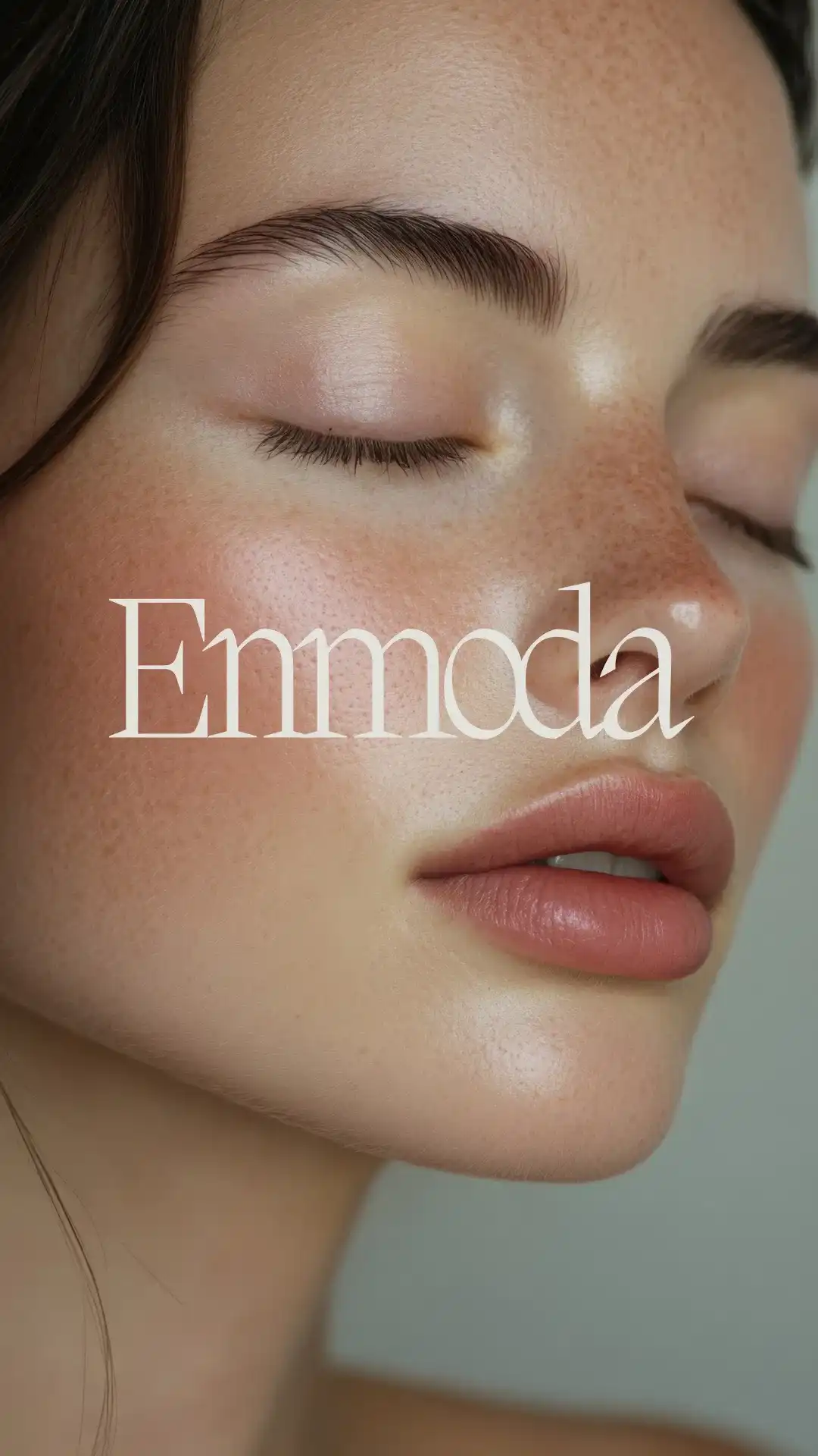 Close-up of a serene face with freckles and closed eyes, overlaid text "Enmoda".
