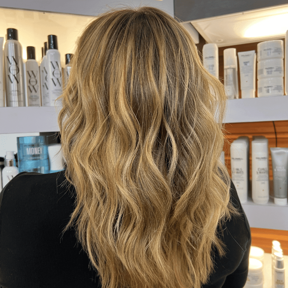 Blonde wavy hair styled in a salon, surrounded by hair products on shelves.