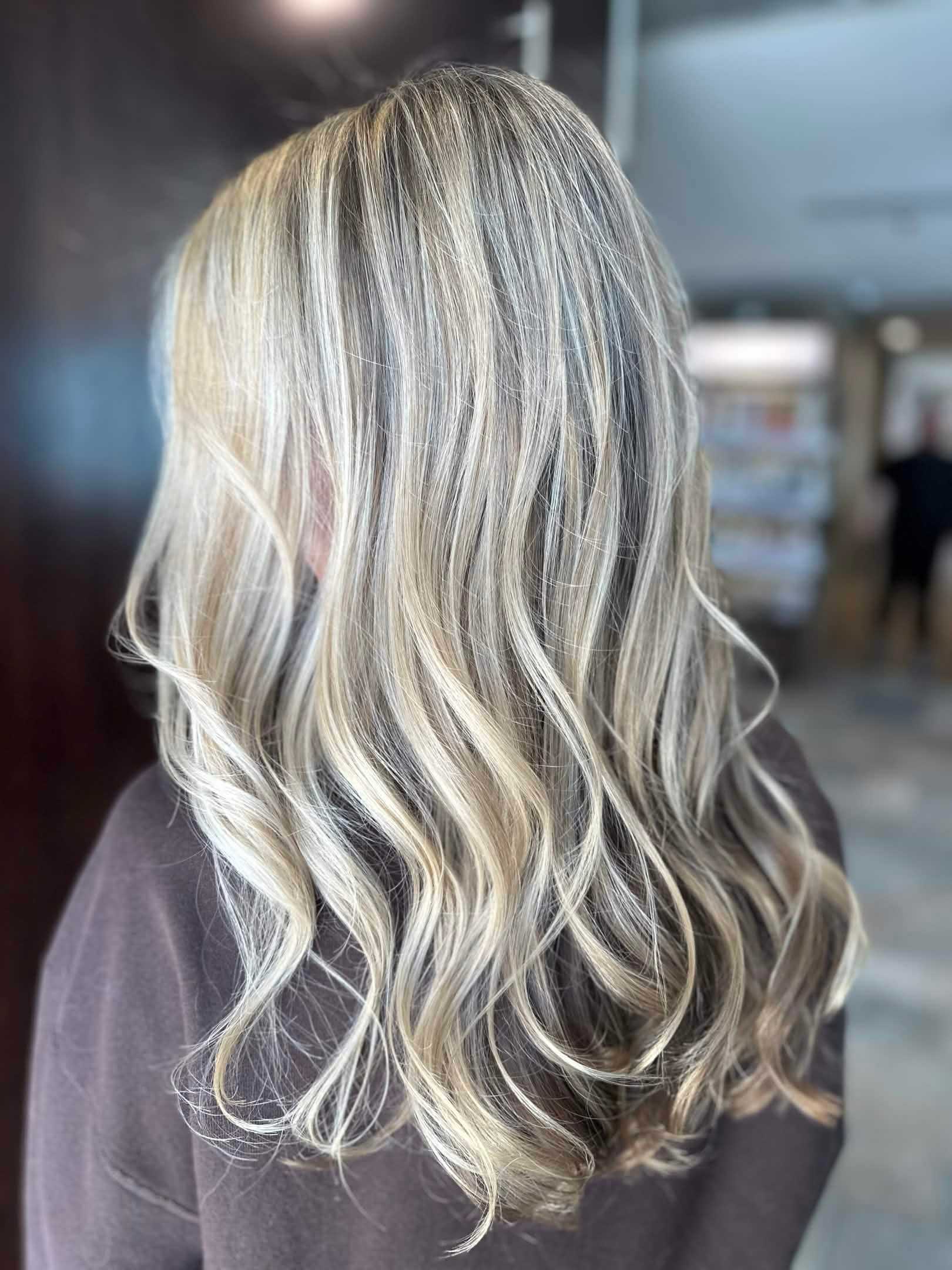 Blonde hair with soft waves and highlights, viewed from the back in a salon setting.