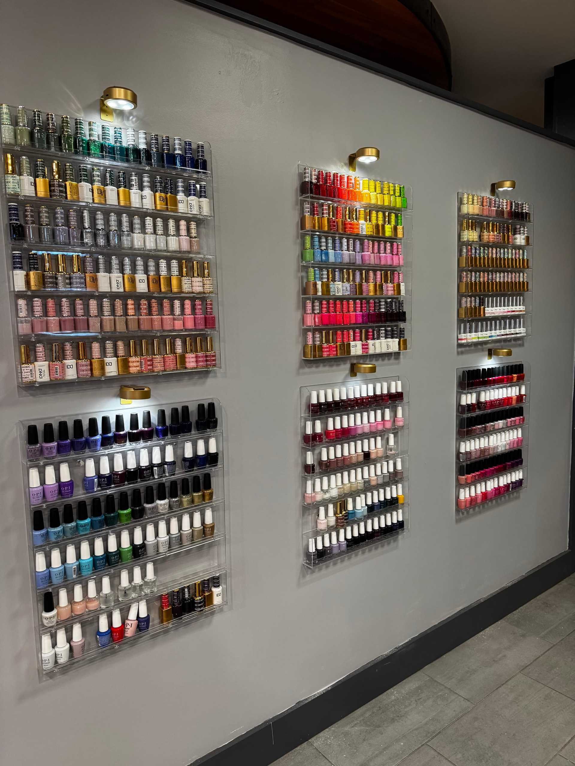 Nail salon wall with colorful nail polish bottles neatly organized in shelves.