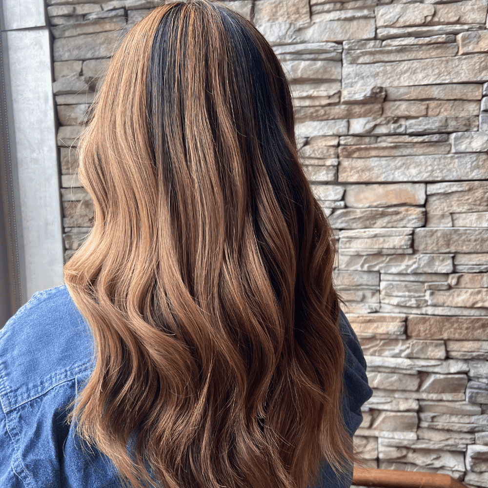 Brown wavy hair against a stone wall backdrop, person wearing a denim shirt.